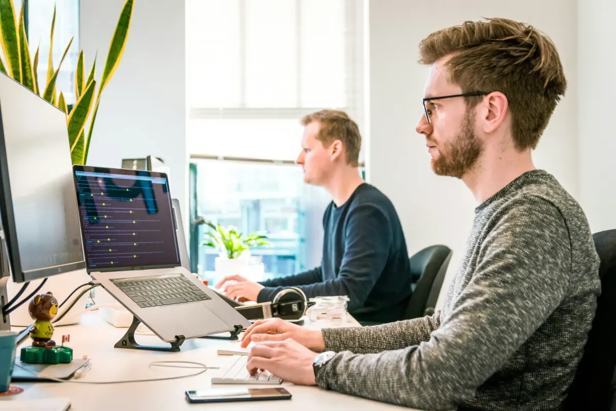 Dois programadores a trabalhar nos seus ecrãs num escritório luminoso